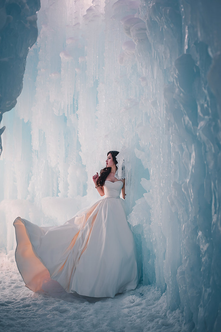 Bride seated inside a blue ice cave in her gown
